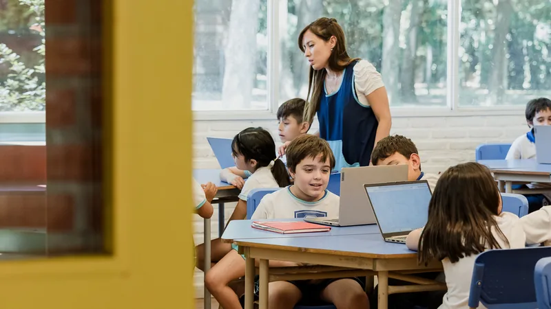Docente y alumnos de primaria trabajando con computadoras portátiles en un aula del Colegio Chesterton.